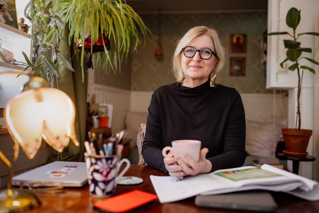 Keski-ikäinen nainen istuu työpöydän ääressä kahvikuppi kädessään.